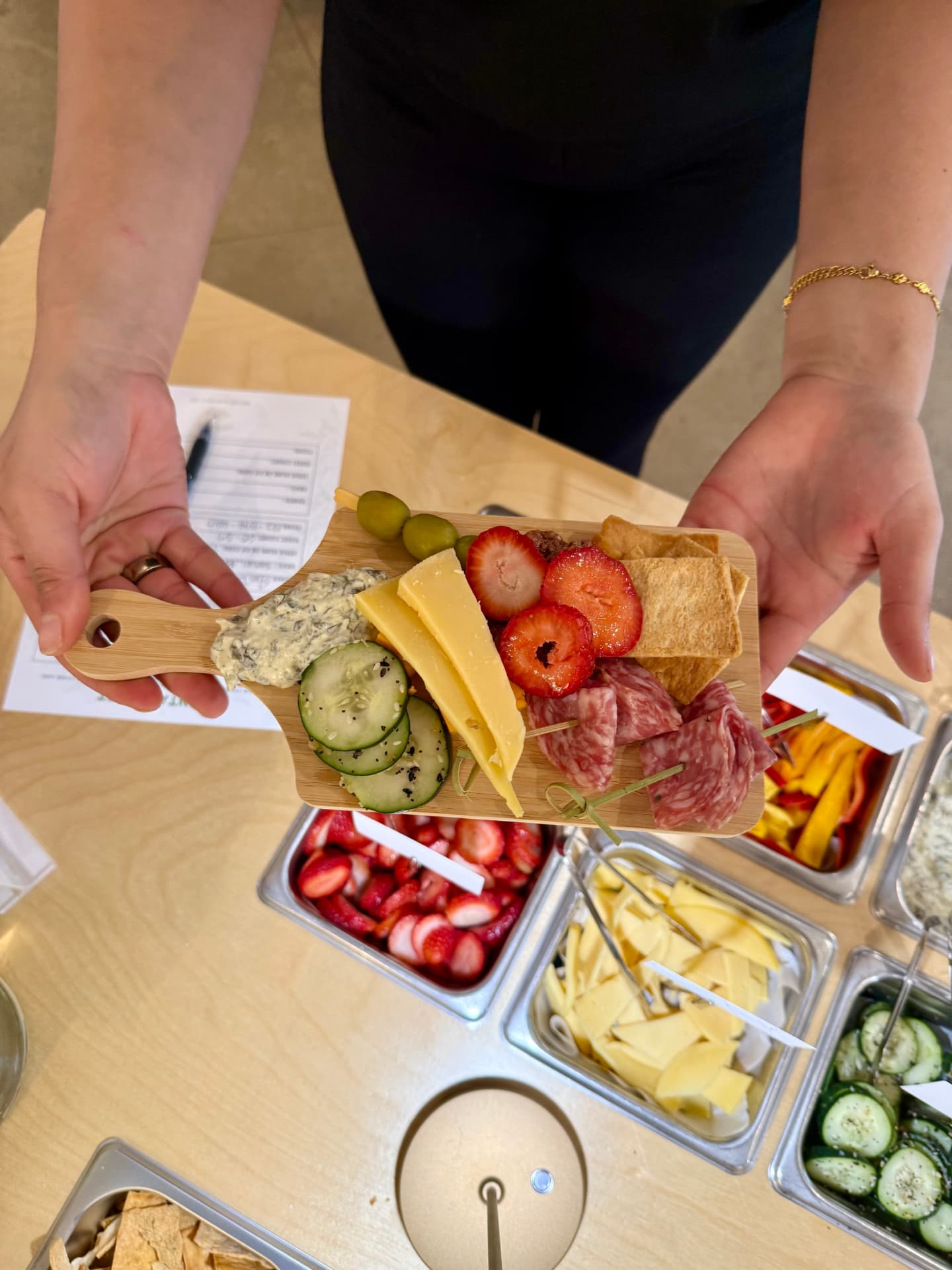 Hands holding a finished board with cheese, strawberries, salami and crackers