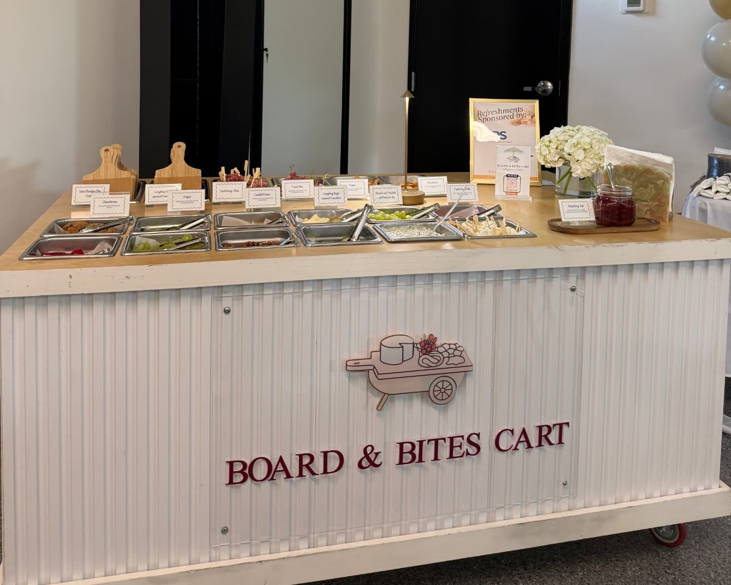 The Board & Bites Cart styled indoors with labeled grazing trays and fresh florals